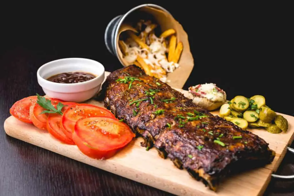 ribs with sliced tomatoes, pickles, and french fries on a board. poolside snacks for summer days